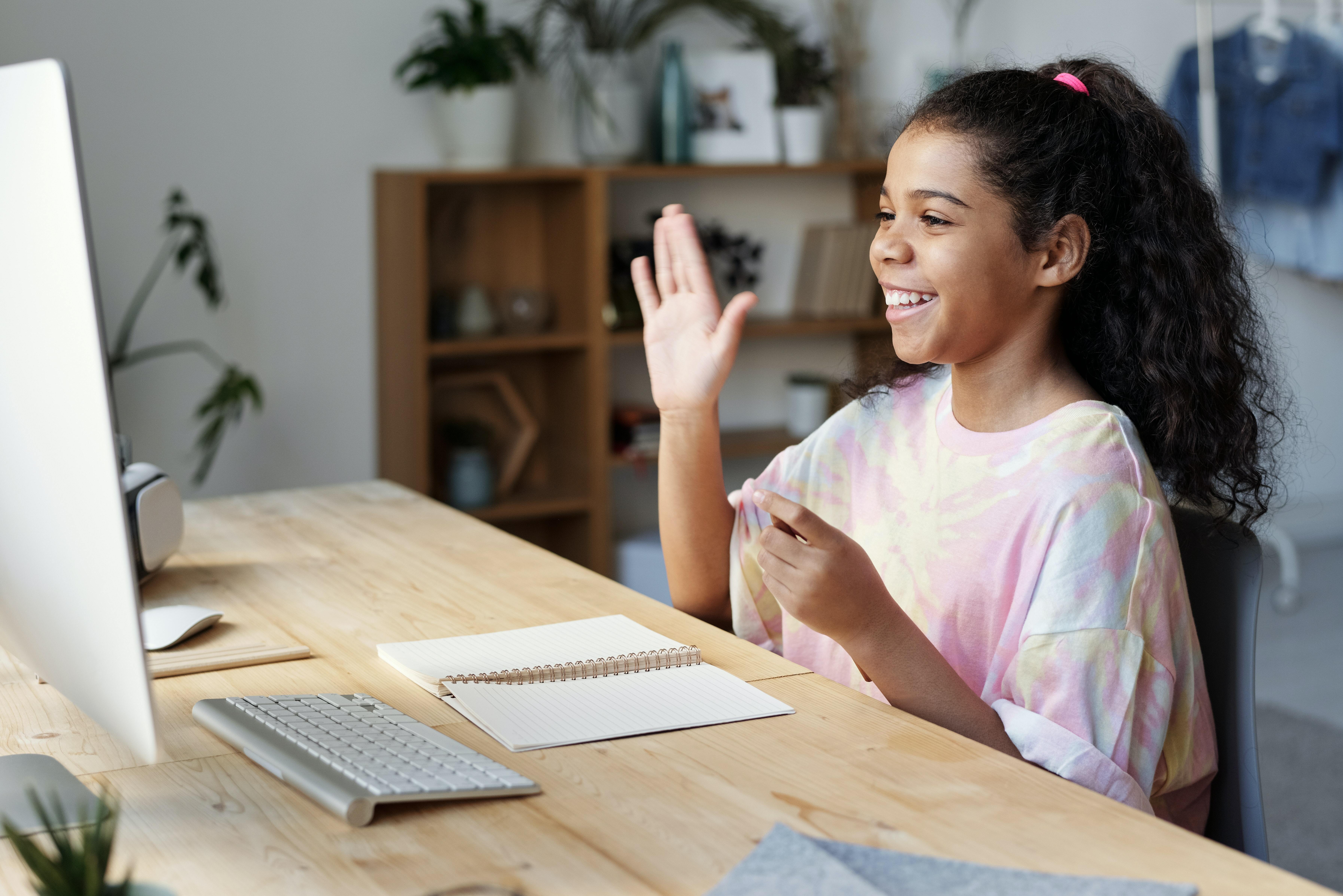 A child smiling during an online meeting and raising her hand.