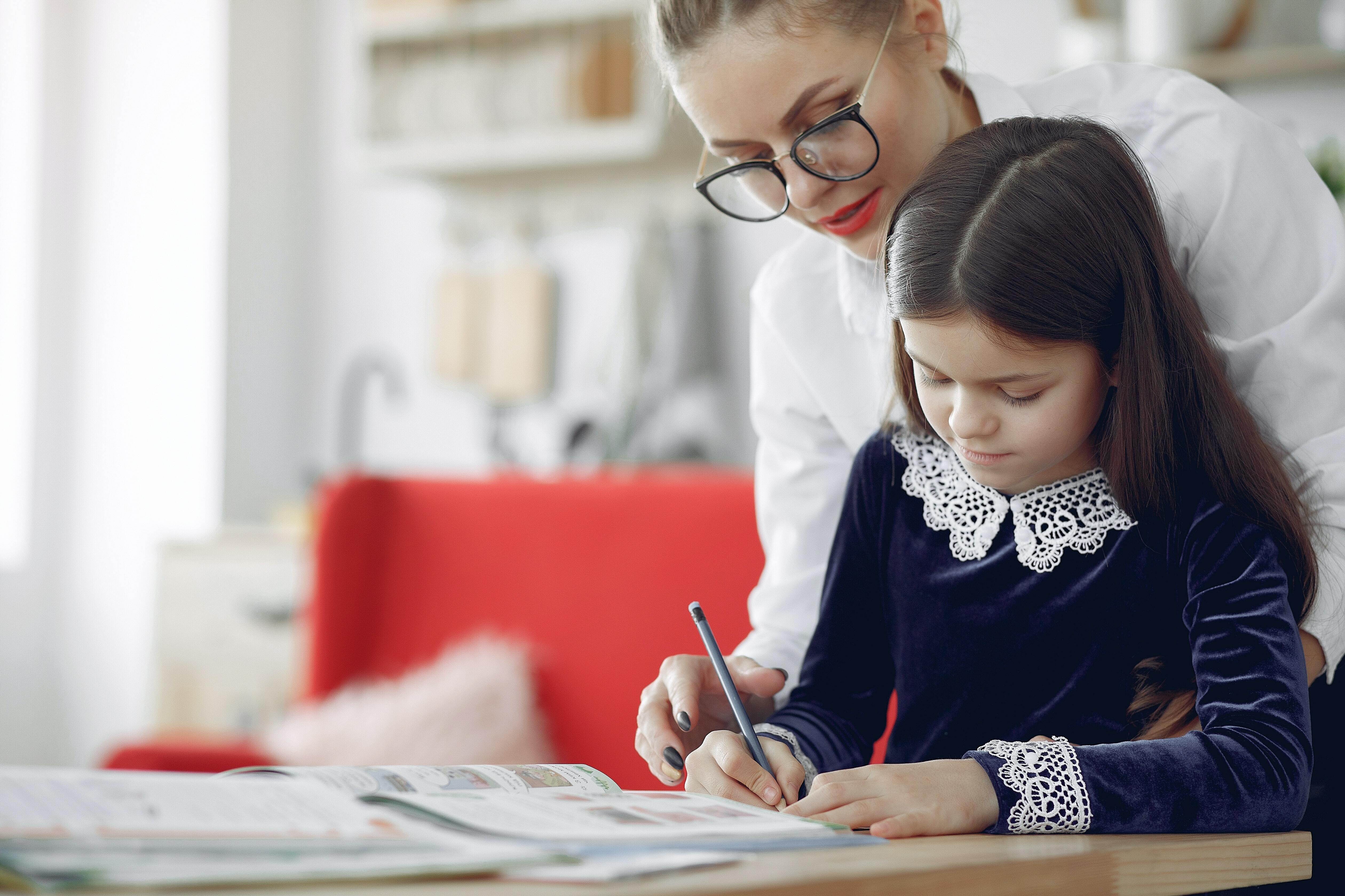 A woman standing over a child writing