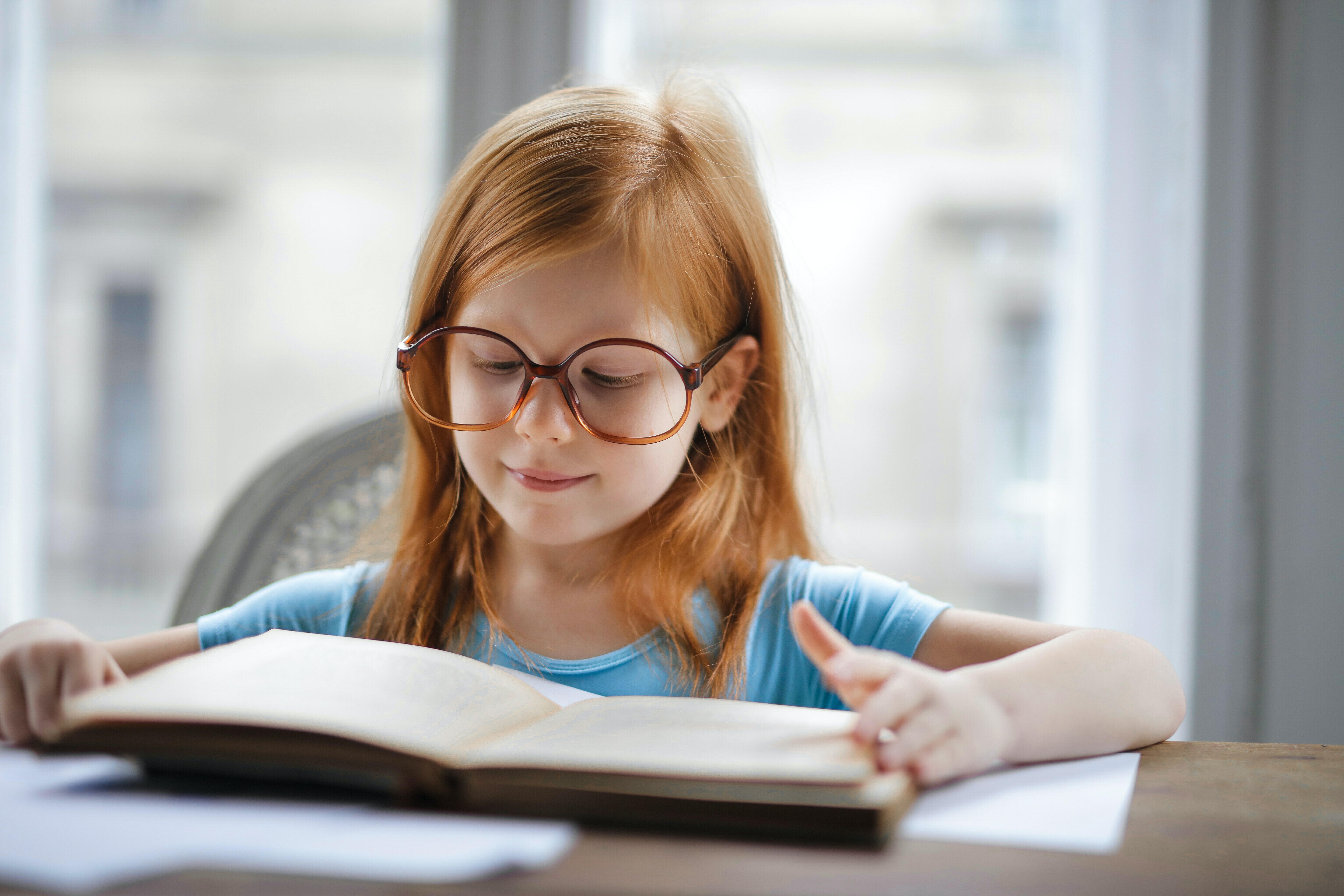 A little female child wearing glasses with book in front