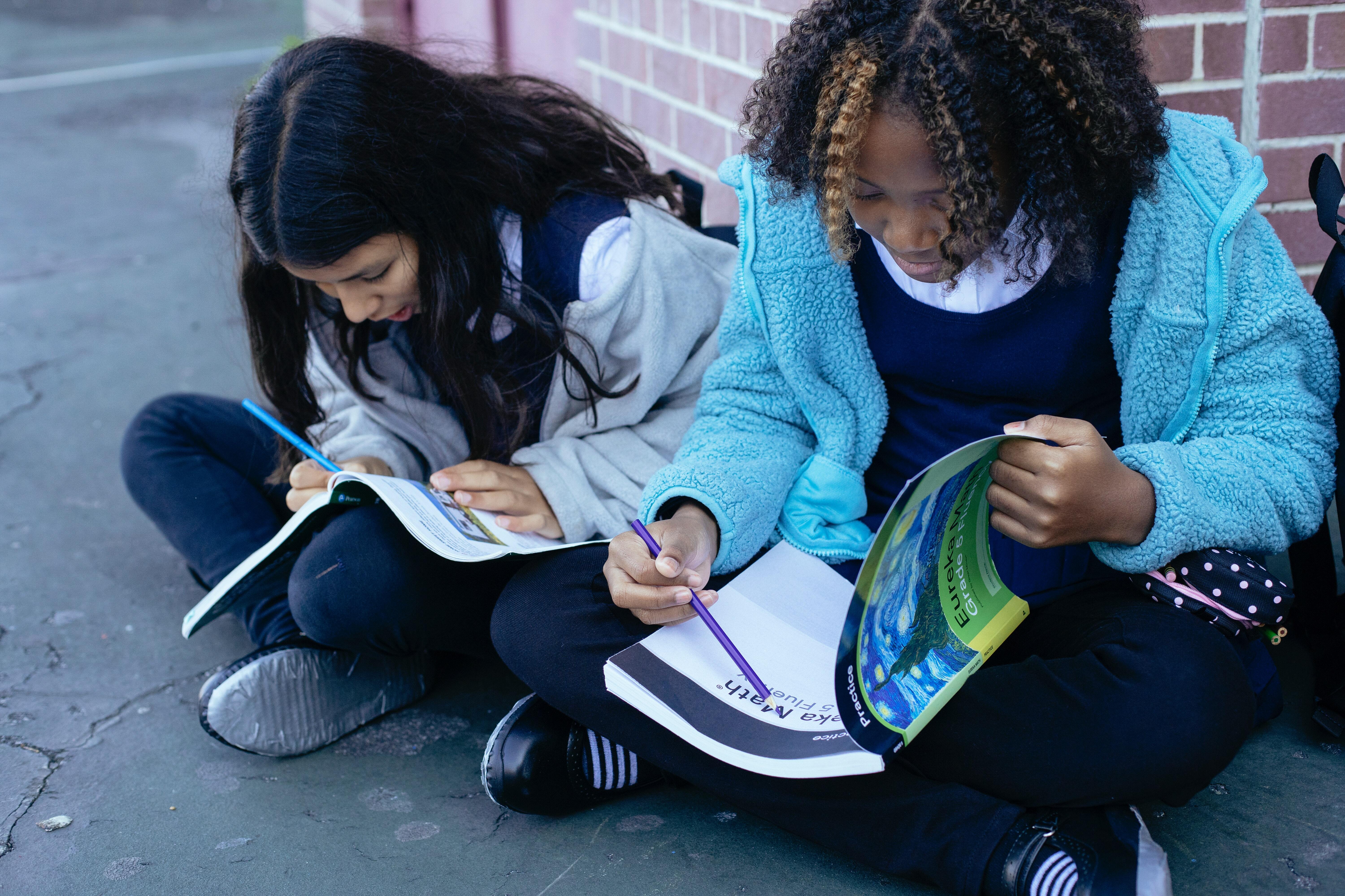 Two school children sitting on the floor while writing