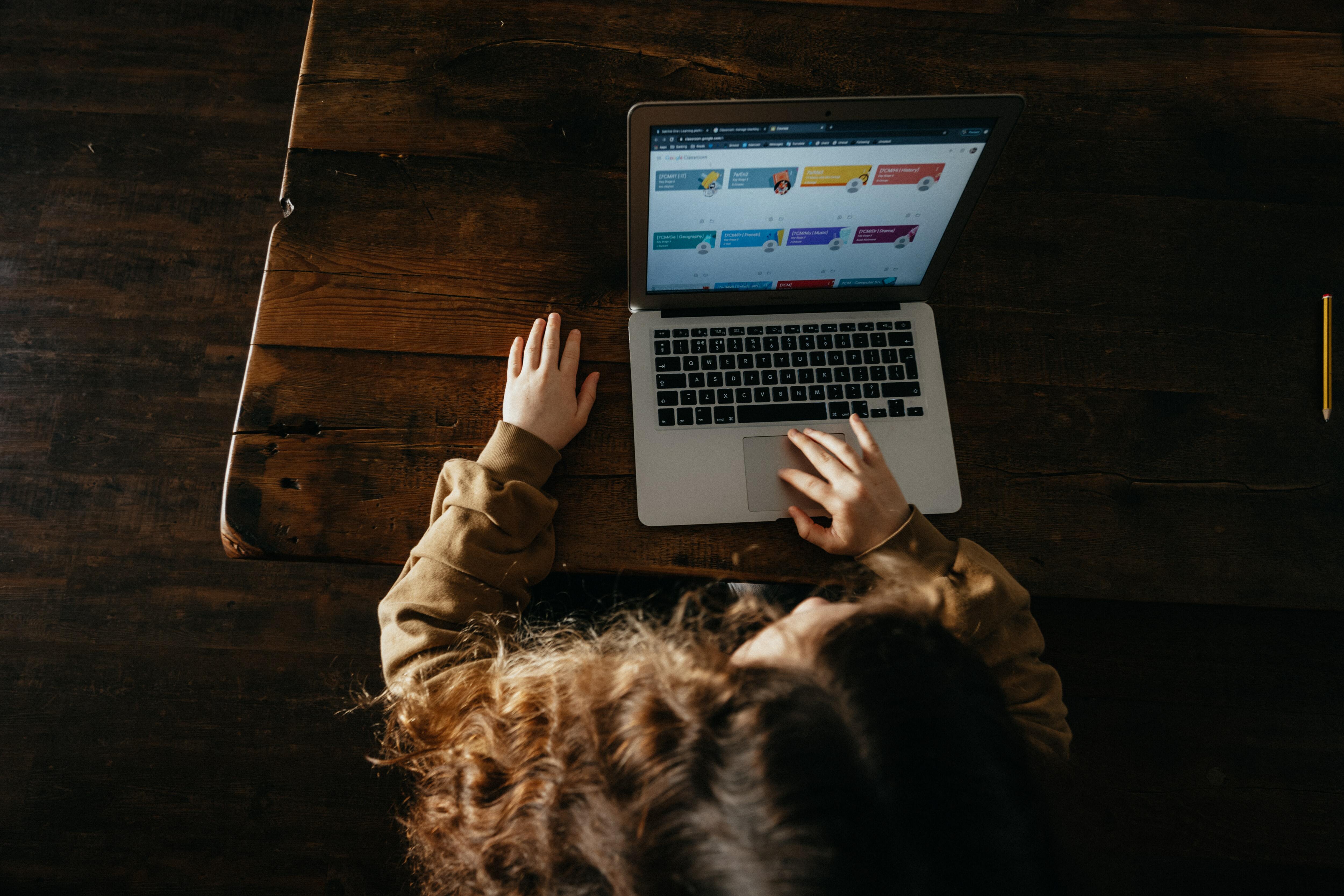 A woman pressing a laptop placed on a wooden table