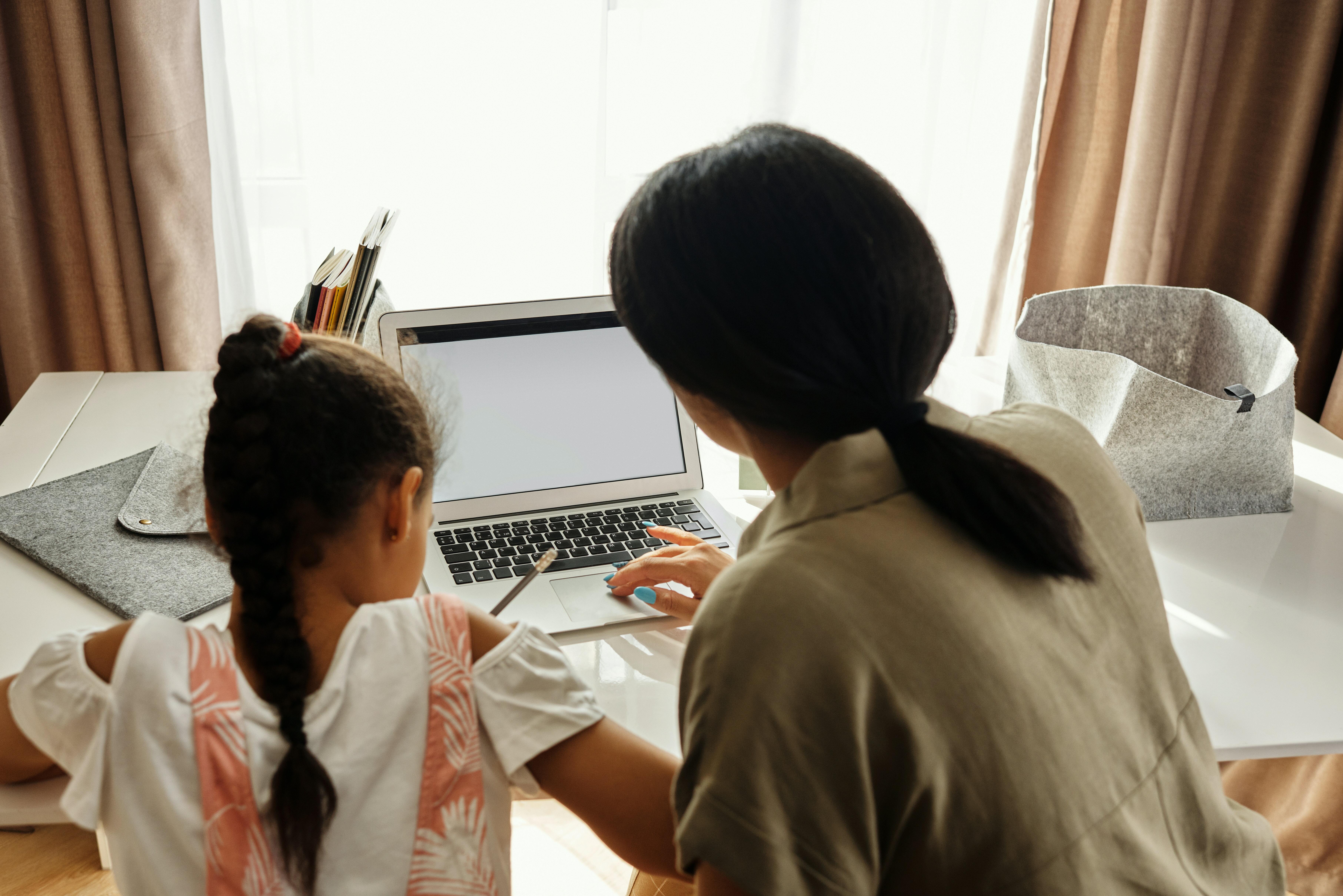 A woman working with a laptop with a little child beside her