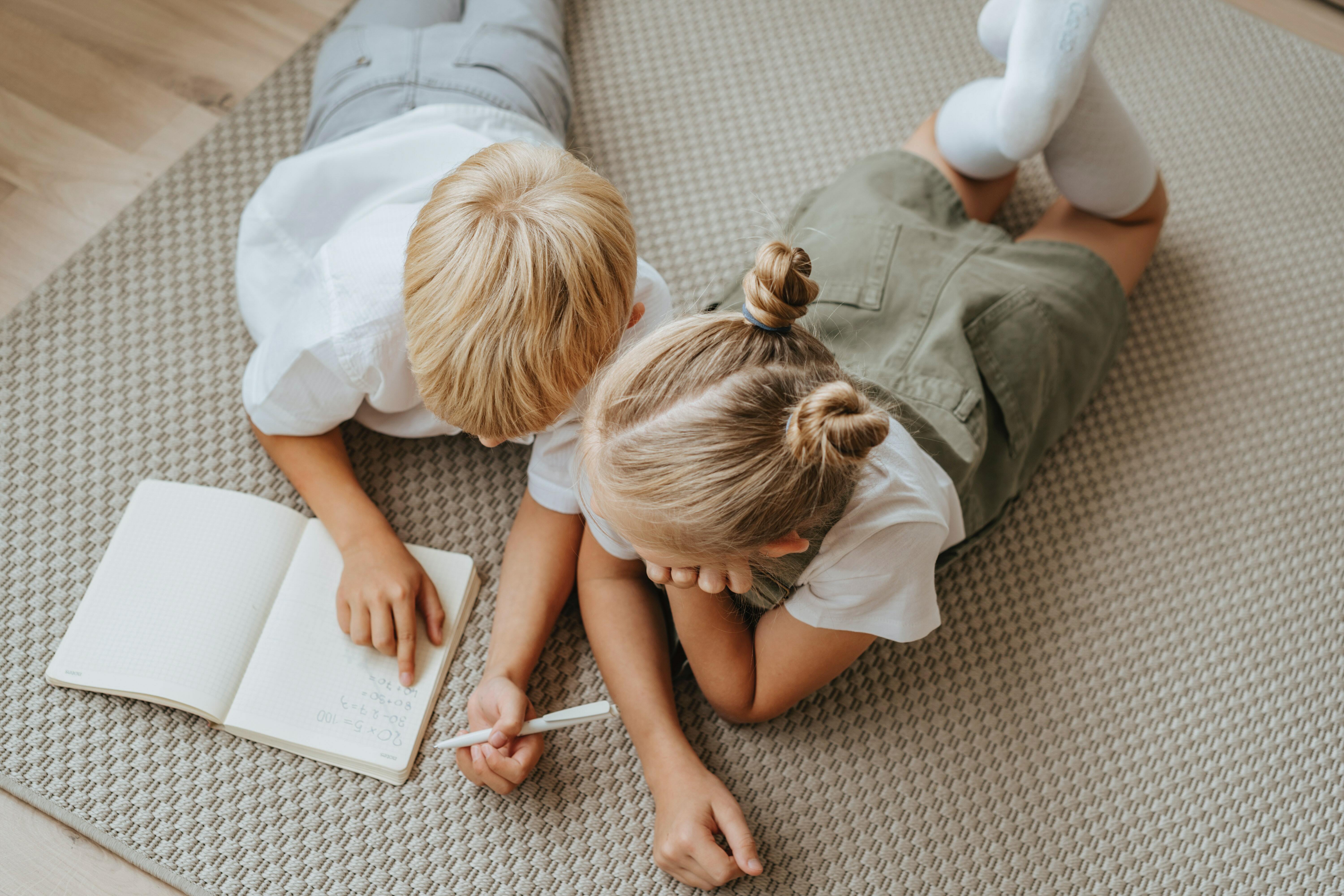 Two children writing on a book on the floor