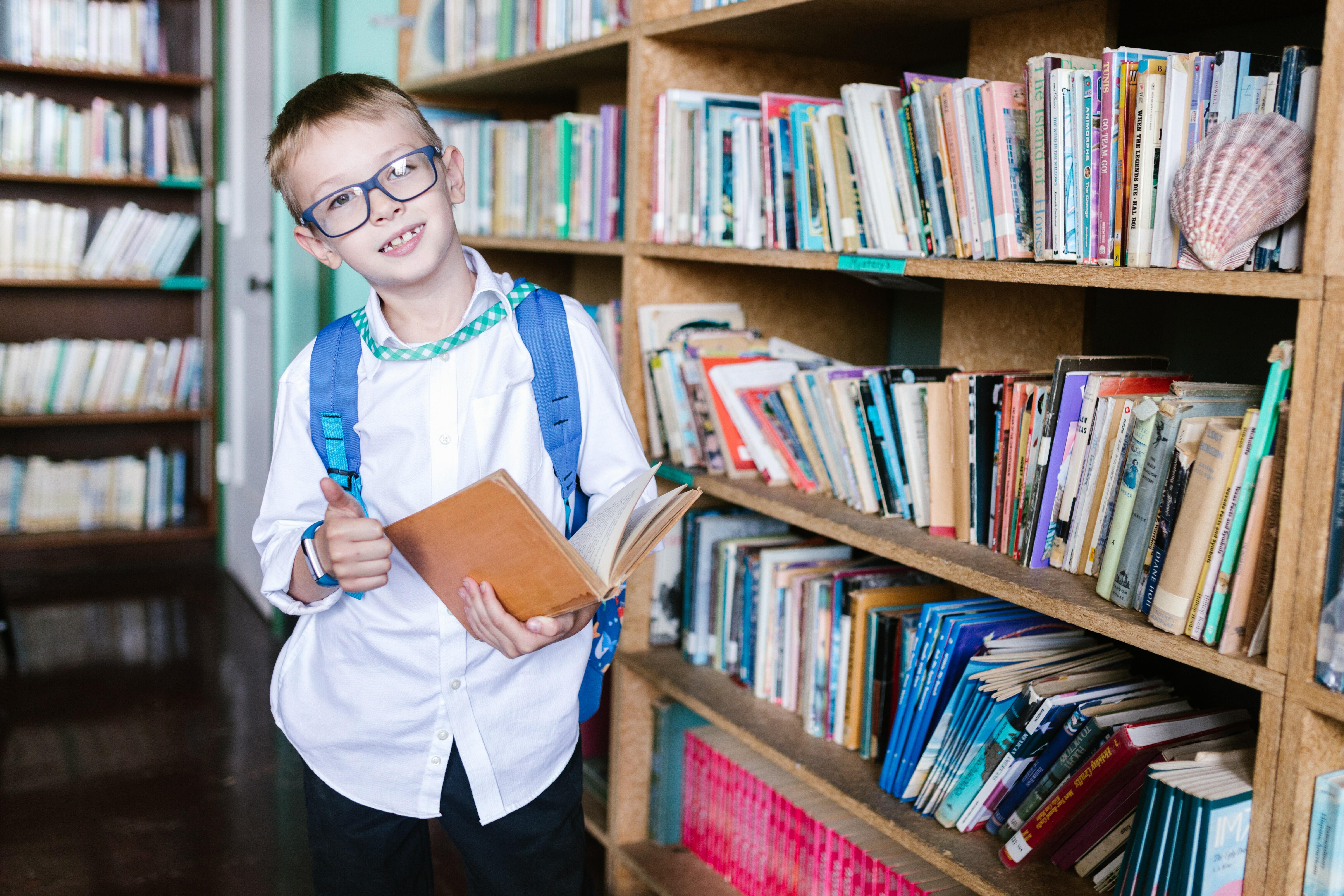 A boy holding a book in a library while standing