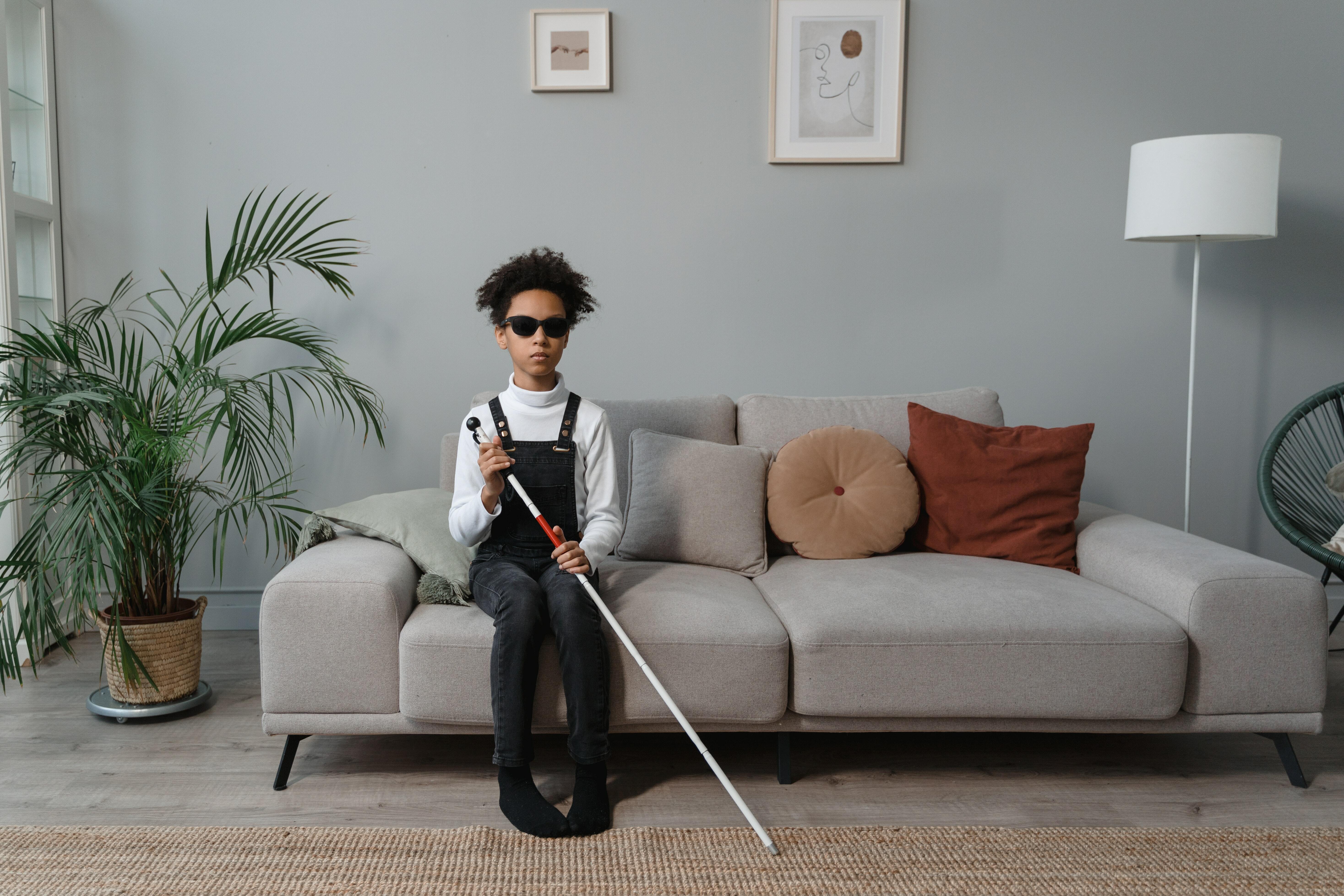 Boy Sitting on Gray Couch Holding a White Cane