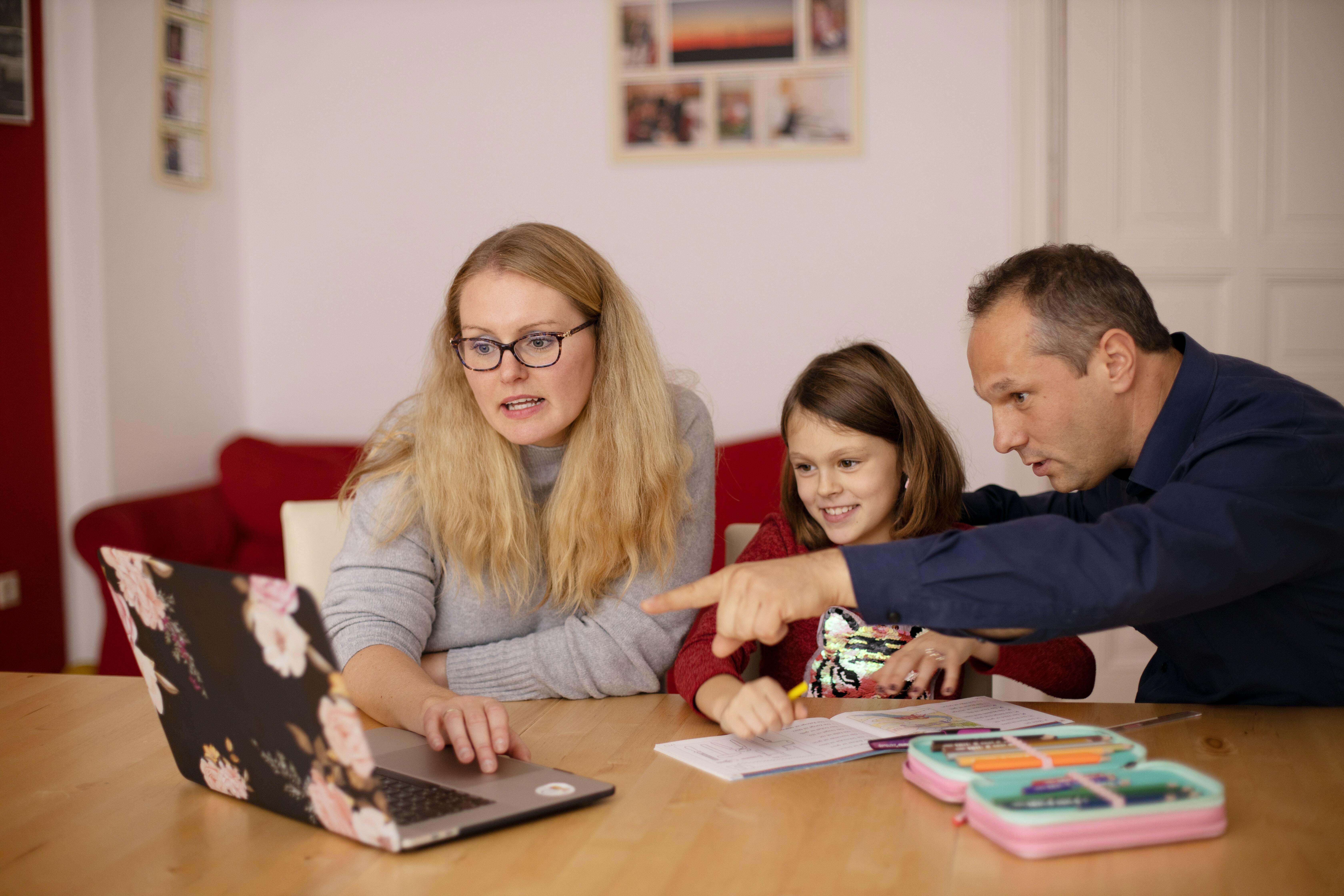 A mother and father homeschooling their child with the father pointing to the screen of the laptop