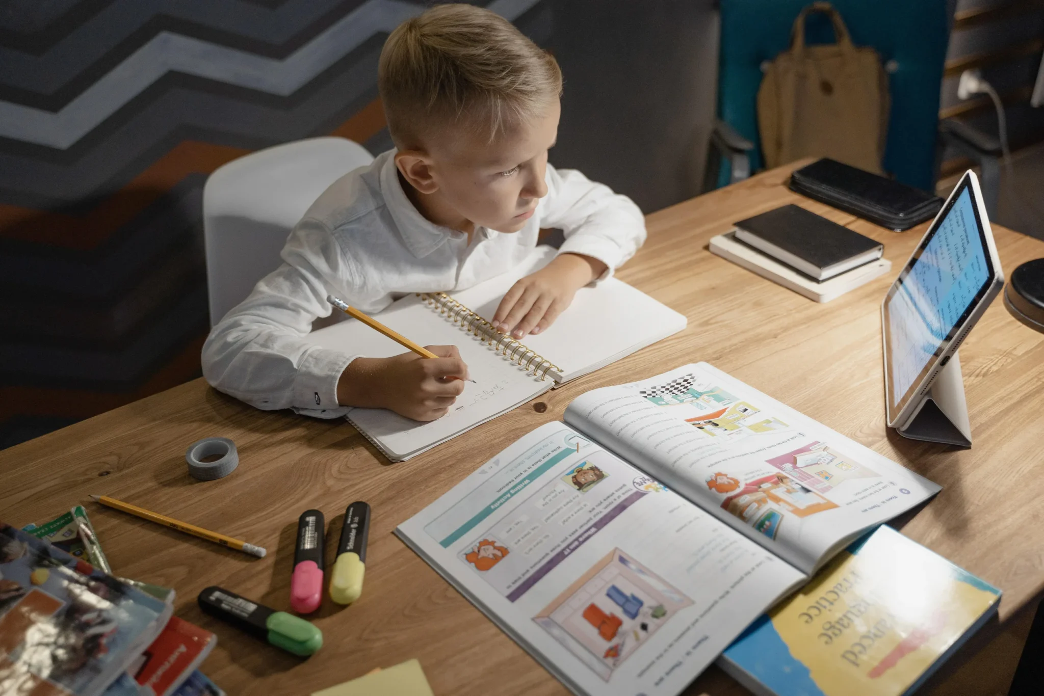 A child taking notes while studying on a tablet and with a book.