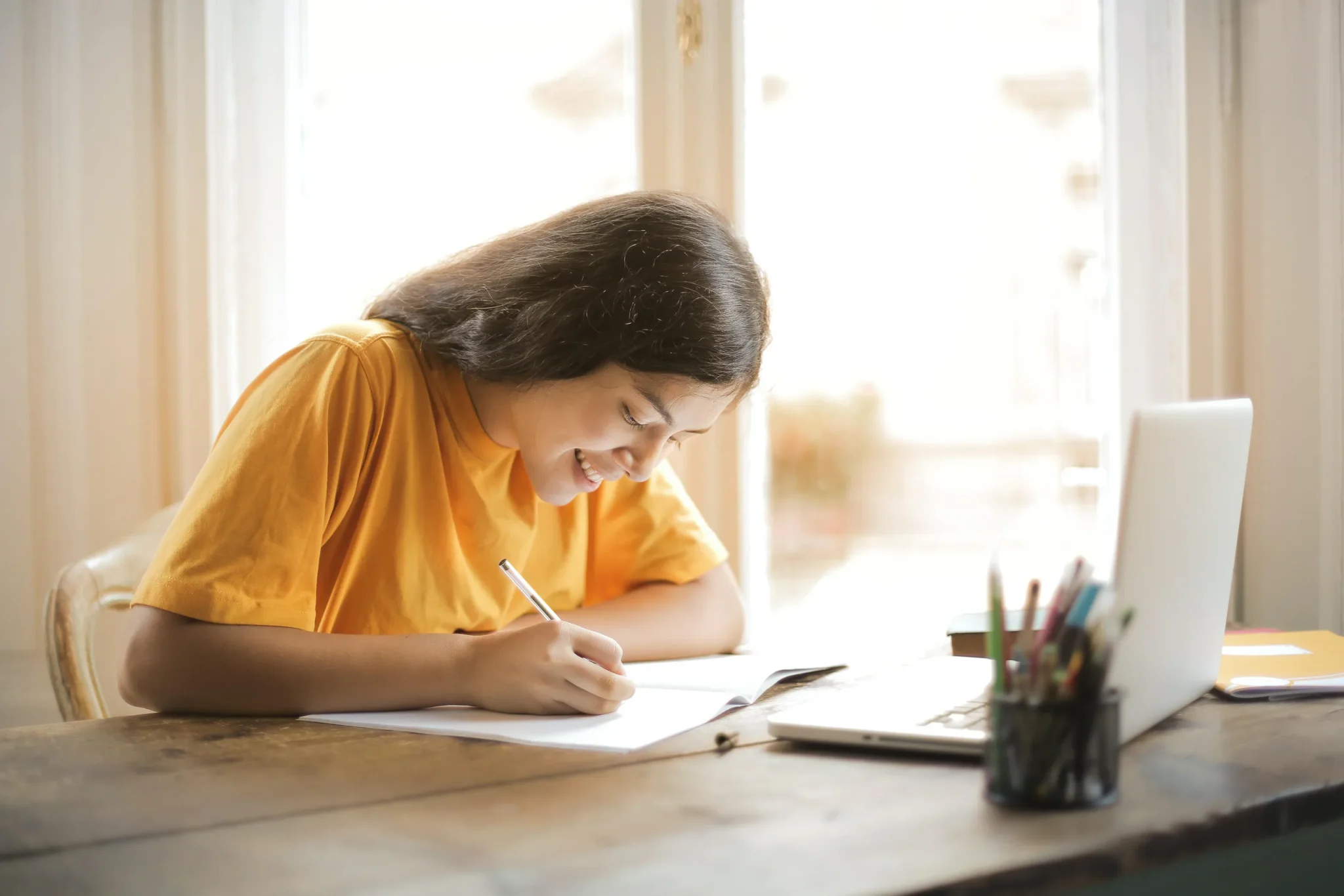 A girl writing in front of a laptop