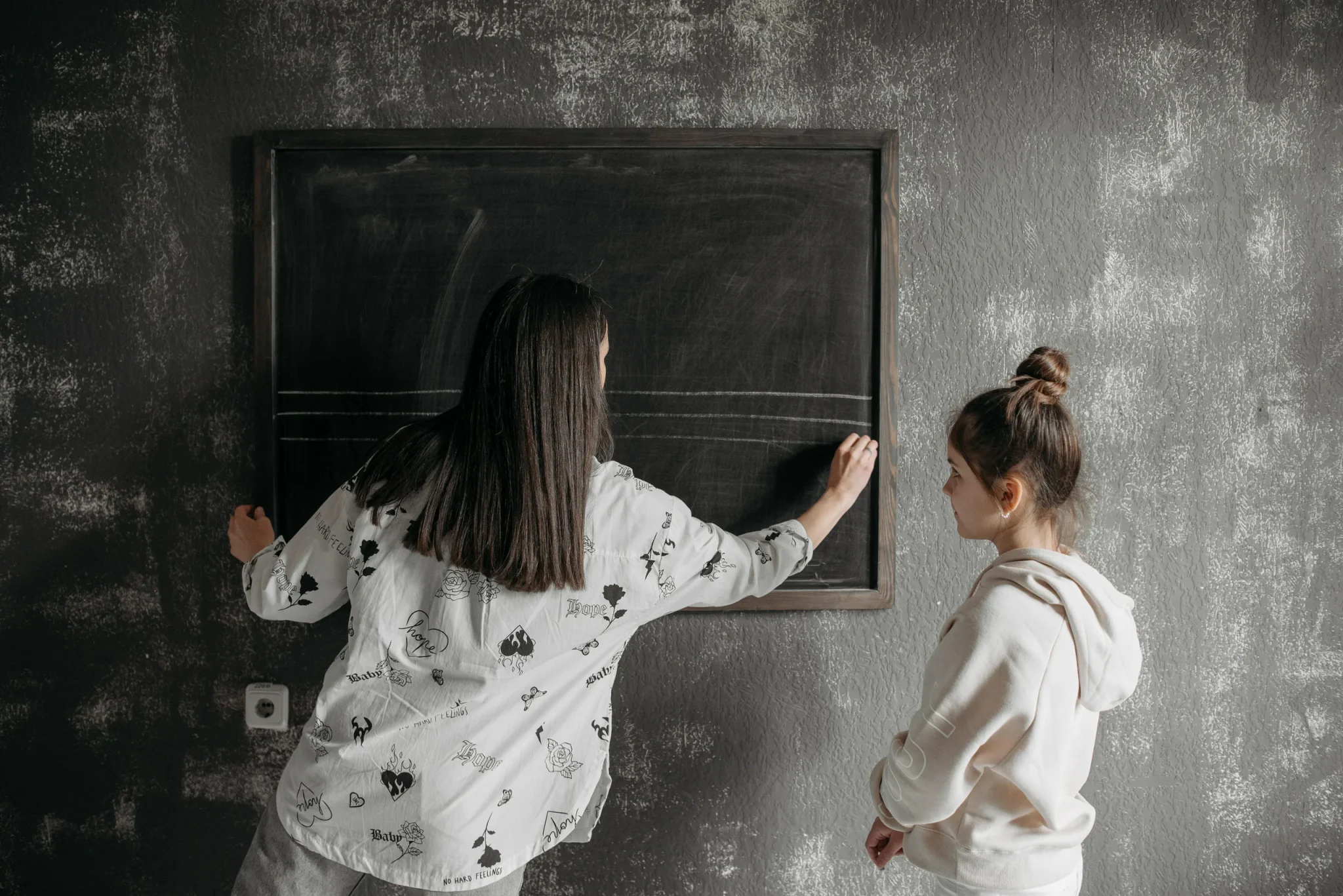 A person writing on a black chalkboard in front of a child