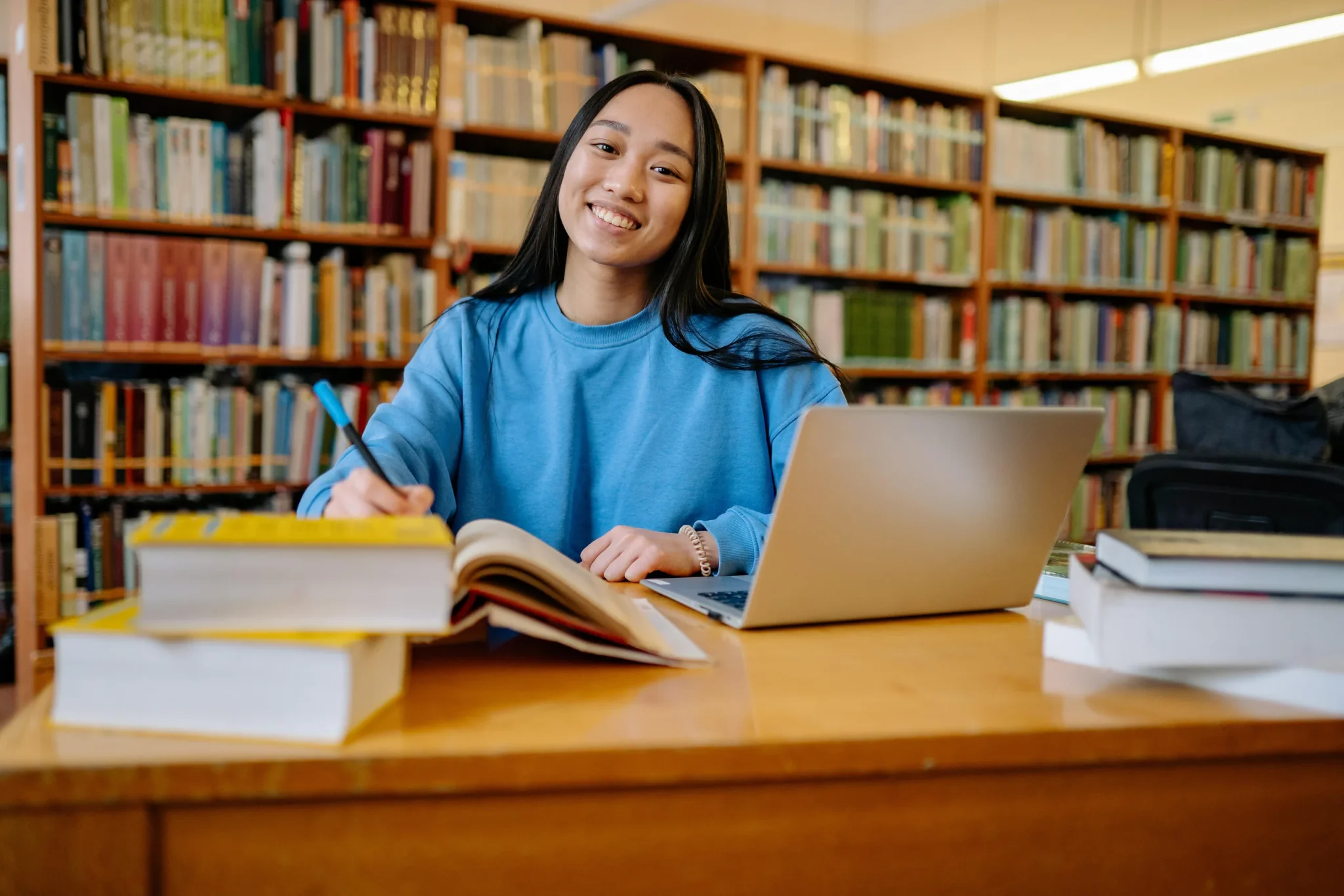 Woman in a library with a laptop and an open book