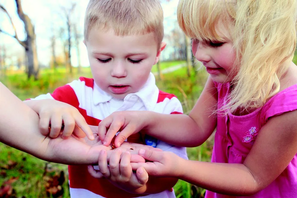 Children touching small insects in parent's hands GHC