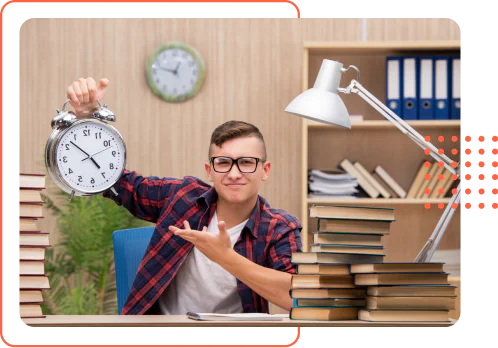 A teenage boy with glasses sitting at a desk piled high with books, holding up a large alarm clock with a frustrated expression