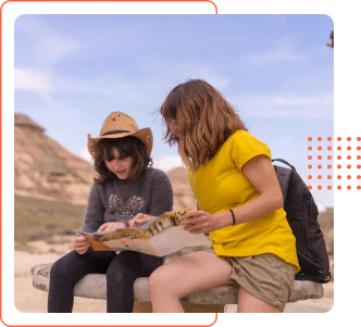 A mother and her young child wearing a hat sitting outdoors in a rocky desert environment, looking down at an open paper map together
