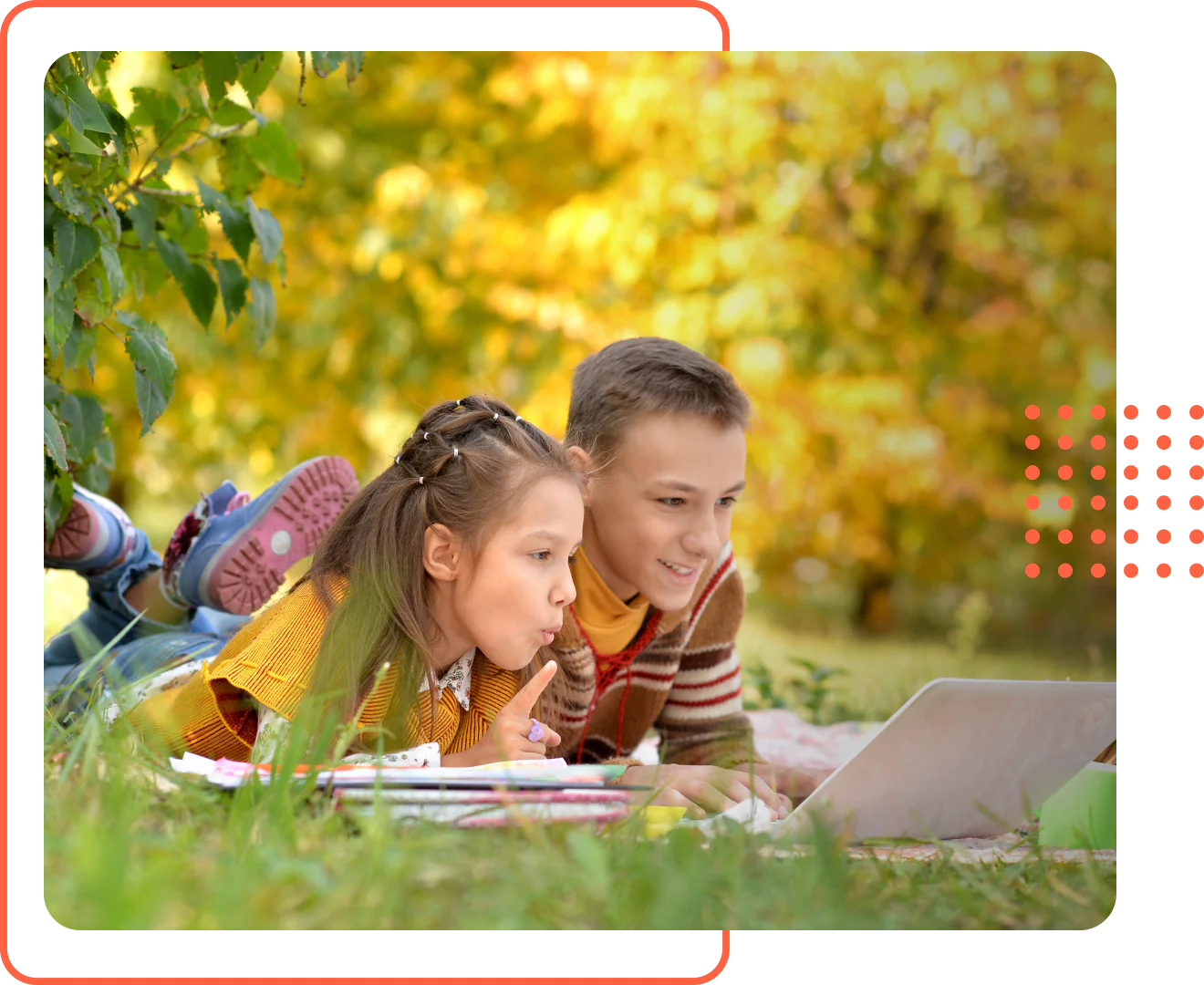 A teenage boy and a younger girl lying in the grass looking at schoolwork during an outdoor homeschool lesson