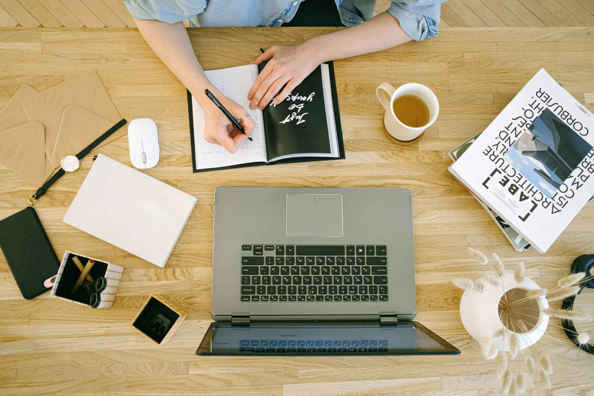 A person holding a pen, writing on notes with laptop in front