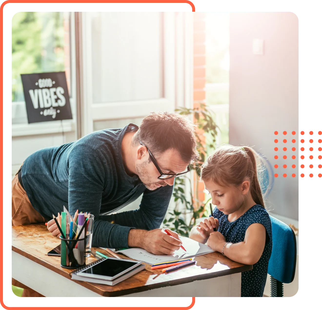 A father leaning over a desk to help his young daughter with her schoolwork during a homeschool lesson